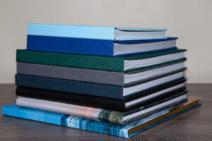 A stack of 8 linen and photo wrap photo books viewed from the spine side on a table